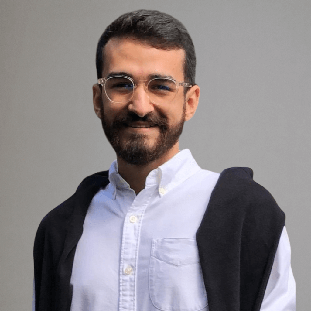 Imagem de perfil de Vitor, Analista do Sucesso do Cliente, com sorriso e vestindo uma camisa branca e um suéter escuro, apresentando um fundo neutro.