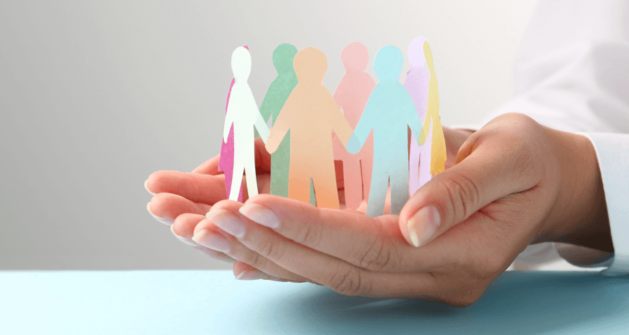 Imagem de mãos segurando figuras de pessoas recortadas em papel colorido, simbolizando união, diversidade e proteção.