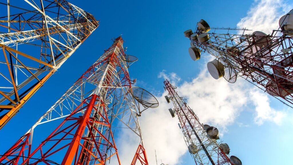 Torres de telecomunicação de alta capacidade contra um céu azul, demonstrando a infraestrutura essencial para comunicação remota.