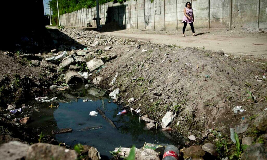 Sistema de drenagem urbano poluído com lixo e água estagnada, refletindo desafios na gestão de resíduos e saneamento.