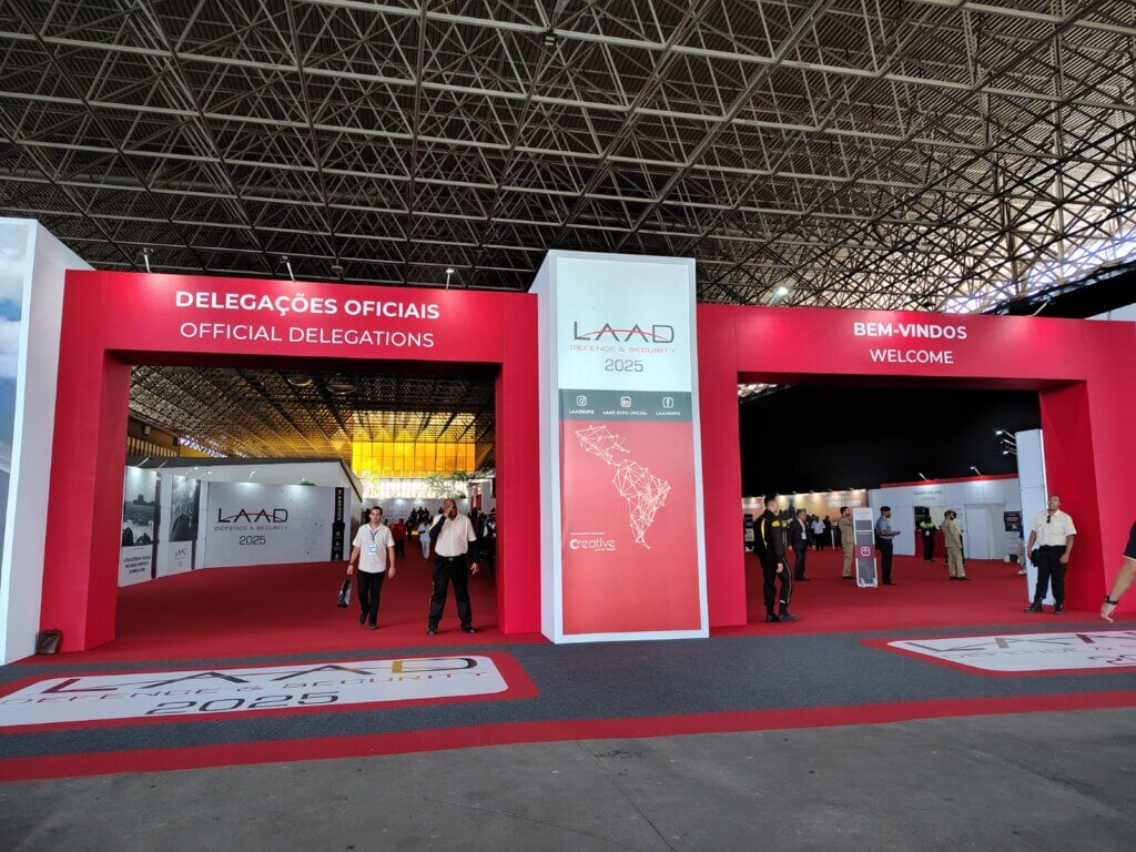 Cena do Riocentro, RJ, durante a feira, com visitantes interagindo com displays e demonstrações ao vivo de soluções geoespaciais, evidenciando a união entre inovação e segurança.