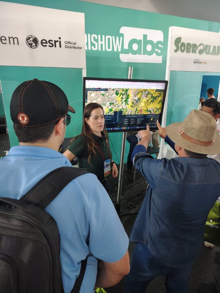 Apresentação de soluções ArcGIS no estande da Imagem Geosistemas durante a Agrishow 2025, com destaque para análise de áreas agrícolas no monitor.