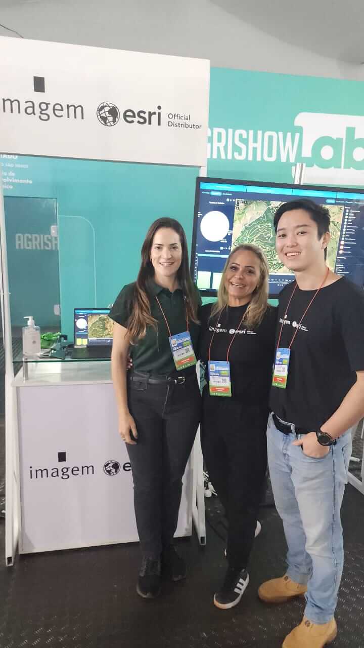 Equipe da Imagem Geosistemas posa no estande da Agrishow 2025, com tela exibindo dashboard do ArcGIS e painel com logo Esri.