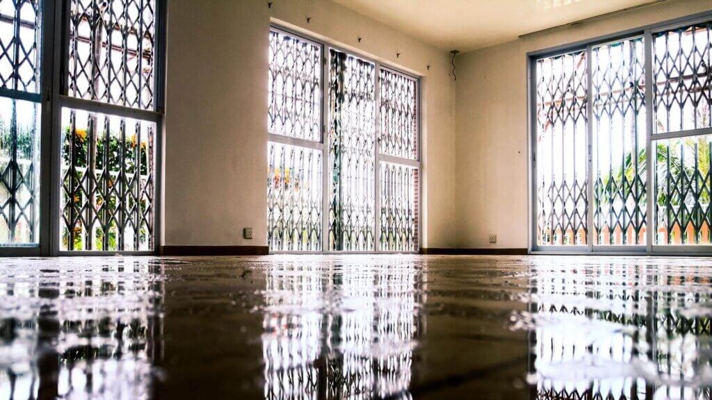 Ambiente interno com piso molhado devido a alagamento, refletindo janelas gradeadas e destacando os riscos de inundações em áreas comerciais.