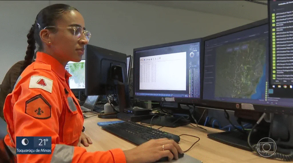 Bombeira militar do Corpo de Bombeiros de Minas Gerais opera sistema de monitoramento com tecnologia ArcGIS em duas telas com mapas interativos e dados em tempo real.