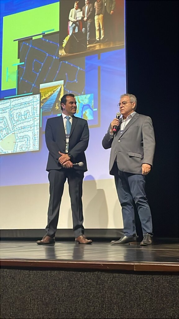 Guilherme Viana, executivo da Imagem, fala ao público com o banner do evento ao fundo e Presidente da CAESB Luis Antonio Almeida Reis