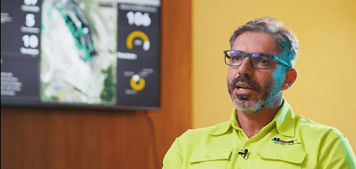 Executivo da Mosaic Fertilizantes durante depoimento sobre o uso do ArcGIS para ganho de eficiência e análise de dados operacionais, com dashboard geoespacial ao fundo.