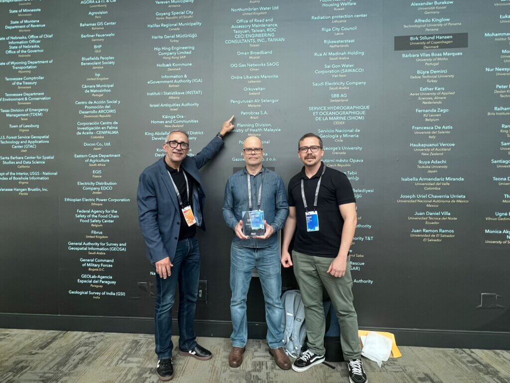 Três profissionais e representantes da Petrobras posam com o troféu do SAG Awards 2025 diante do mural de homenagens da Esri UC, em San Diego.