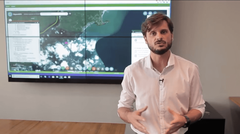 Representante da SIMA-SP apresenta o uso do ArcGIS no monitoramento ambiental e prevenção de queimadas, com mapa interativo e imagens de satélite exibidas ao fundo.