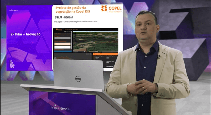 "Apresentador em estúdio com telões ao fundo mostrando o projeto de gestão da vegetação na Copel DIS, com tela do ArcGIS exibindo análise de relevo e informações geoespaciais. Slide destaca o '2º Pilar – Inovação' no Encontro de Usuários Esri Brasil 2023."
