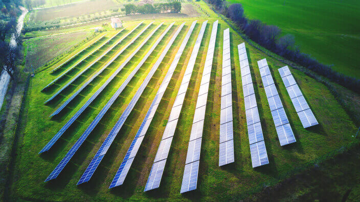 Vista aérea de uma fazenda solar com fileiras de painéis fotovoltaicos organizados sobre o campo verde, representando energia limpa e sustentabilidade ambiental.
