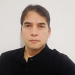 Retrato de Evandro Meireles, especialista em ArcGIS Utility Network, vestindo camisa preta e posicionado em frente a uma parede branca.