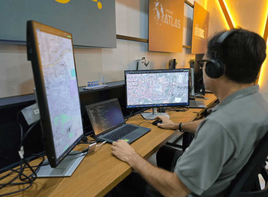 Especialista do Projeto Atlas opera softwares GIS com múltiplas telas em ambiente de monitoramento e desenvolvimento técnico.