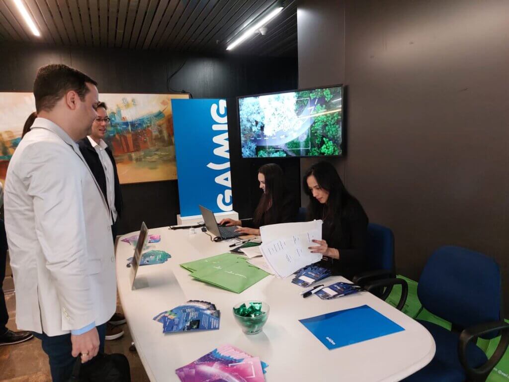 Recepção do 3º GIS Day Gás com equipe da Gasmig realizando credenciamento dos participantes, mesa com materiais e banner da Gasmig ao fundo.