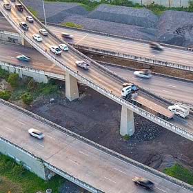 Vista aérea de um complexo de intercâmbios rodoviários com intenso tráfego de veículos. A imagem representa redes de distribuição e logística otimizadas por GIS, destacando a importância da análise geográfica no transporte de bens e pessoas.