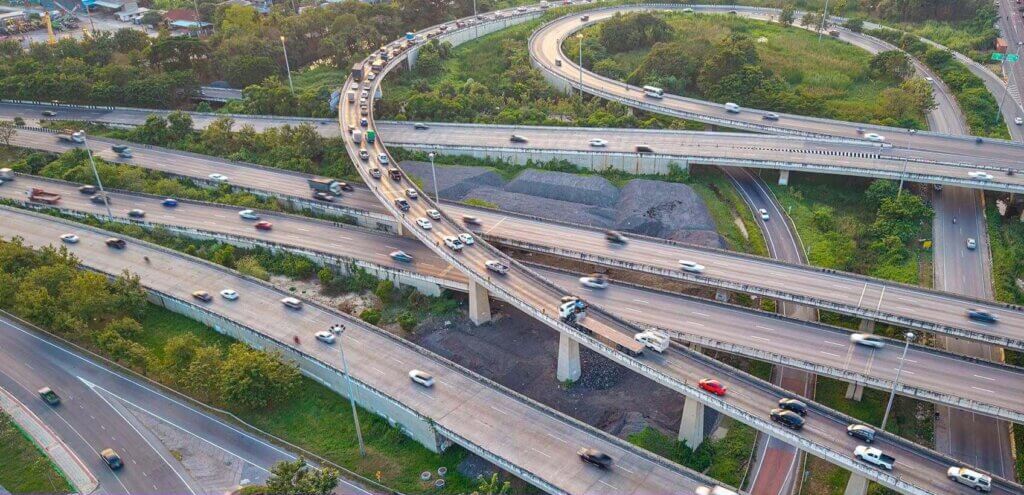 Vista aérea de um complexo de intercâmbios rodoviários com intenso tráfego de veículos. A imagem representa redes de distribuição e logística otimizadas por GIS, destacando a importância da análise geográfica no transporte de bens e pessoas.