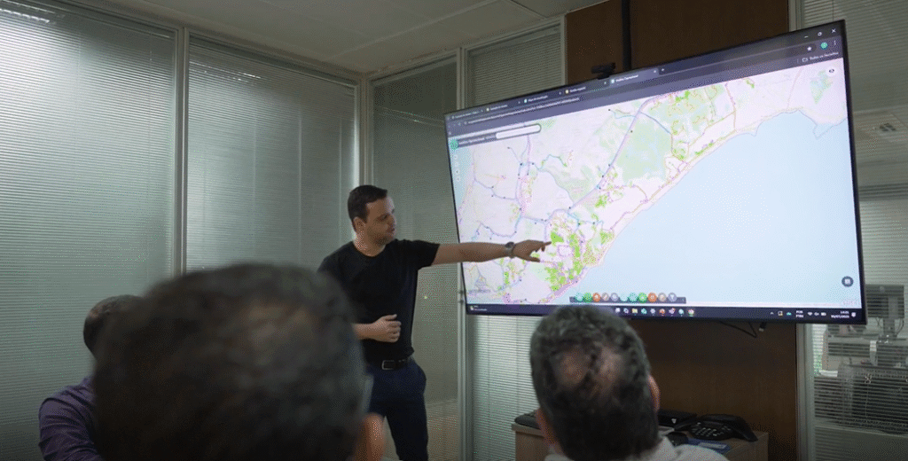 Profissional da Bahiagás apresenta mapa digital interativo em tela grande durante reunião de planejamento estratégico com uso do ArcGIS.