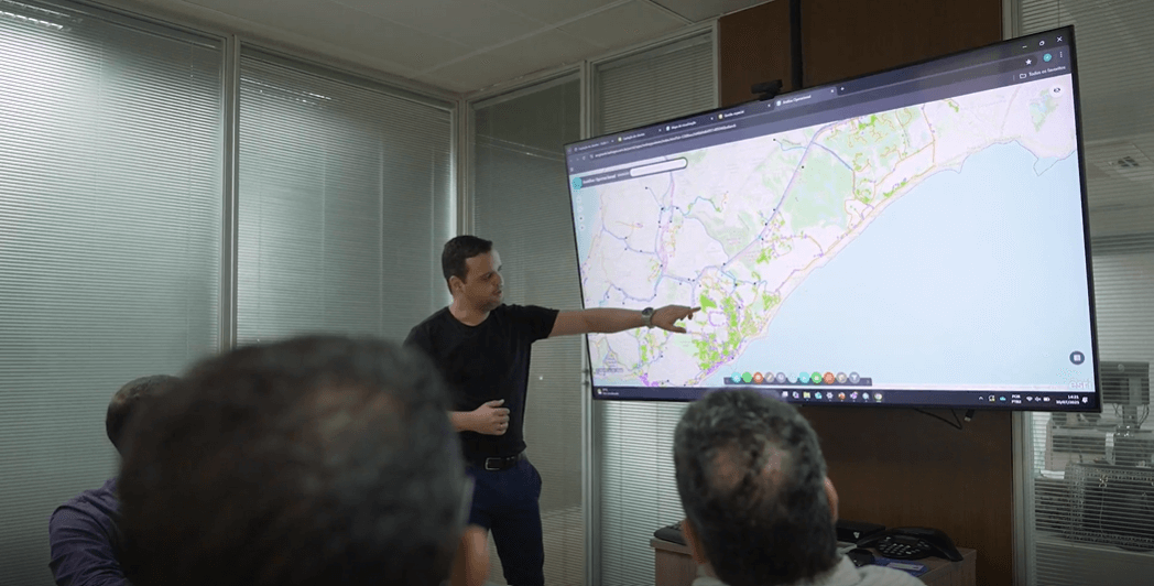 Profissional da Bahiagás apresenta mapa digital interativo em tela grande durante reunião de planejamento estratégico com uso do ArcGIS.